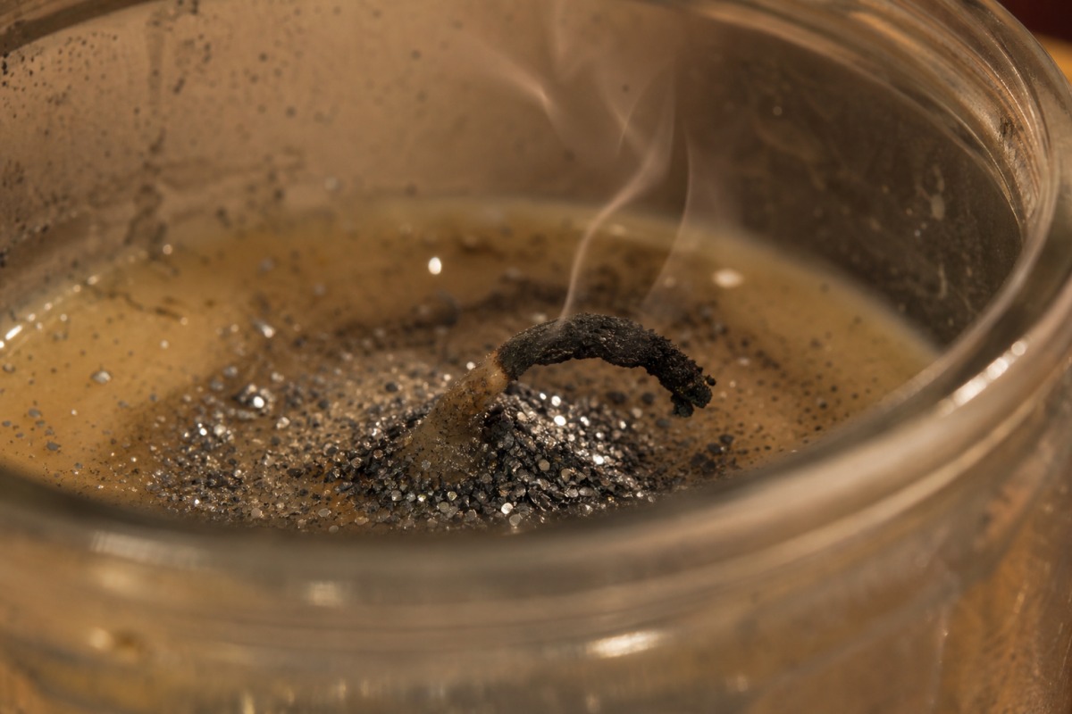 Abgeknickter verkohlter Docht, umhüllt von angesammeltem silbernem Glitter im erstarrten Wachs, die Kerze ist erloschen.