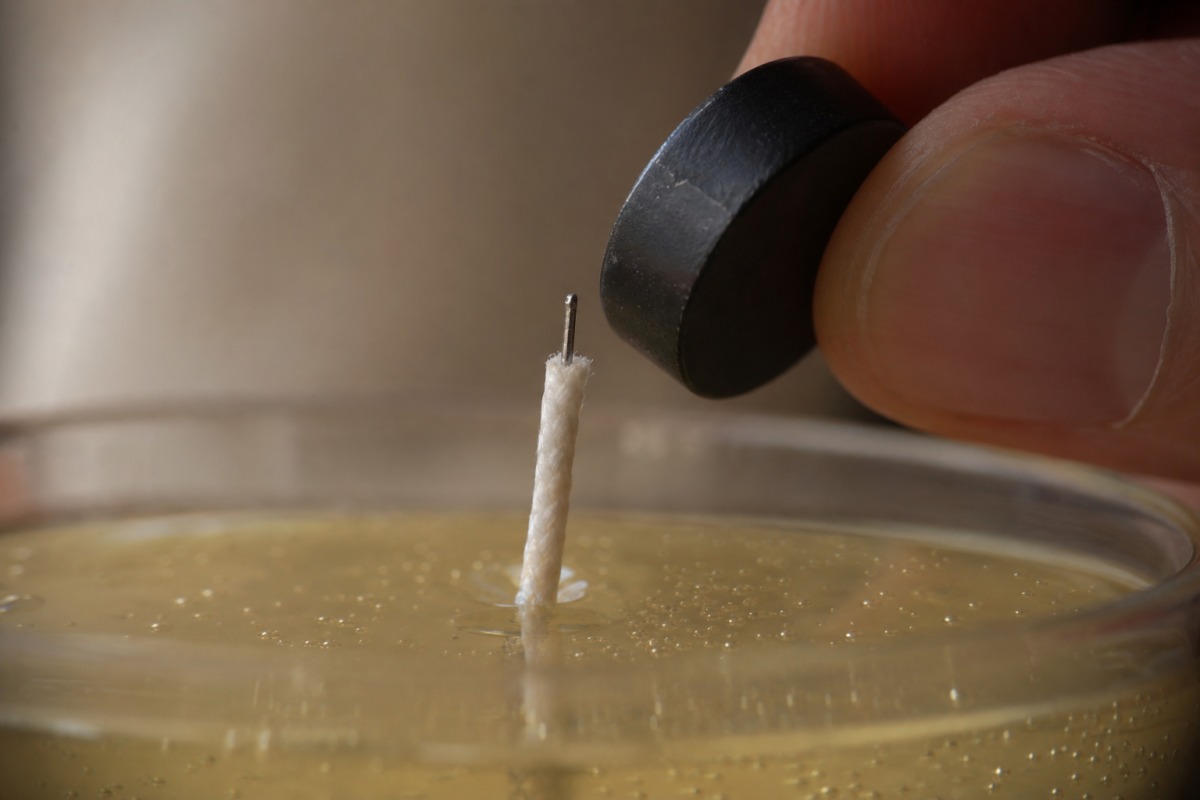 Nahaufnahme eines herausgezogenen Dochts mit dünner Metalleinlage und einem kleinen Magneten dicht am Metallkern des Dochts